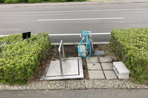 てんとらんどオートキャンプ場：植え込みの間の金属のふたと、ホースのついた水道